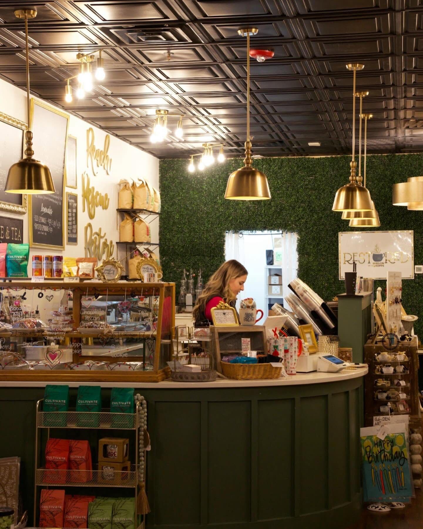 Inside the shoppe: brass pendant lights over the coffee counter and pastry case, with Reach, Rescue, Restore lettered on the wall